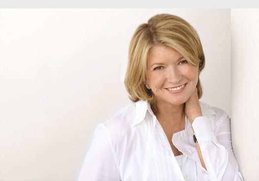Martha Stewart wearing an all-white outfit smiles at the camera. The background is an off white just darker than Stewart's outfit.