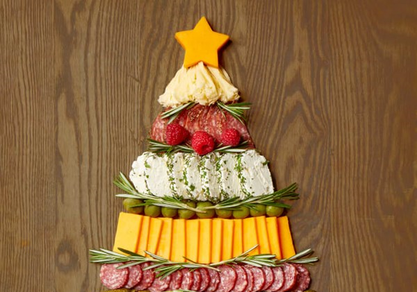 Rows of cheese squares and circles of cured meats are arranged in an elongated triangle to resemble a Christmas tree. Sprigs of rosemary are tucked between each row, and a star-shaped piece of cheese tops the "tree"