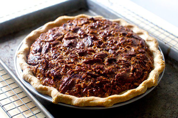 Closeup of a dark golden brown pecan pie with pecan halves on the top and a loosely crimped crust.