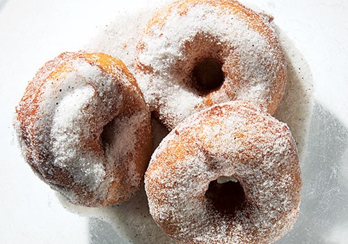 three sugar-dusted cake donuts sitting in a bed of sugar