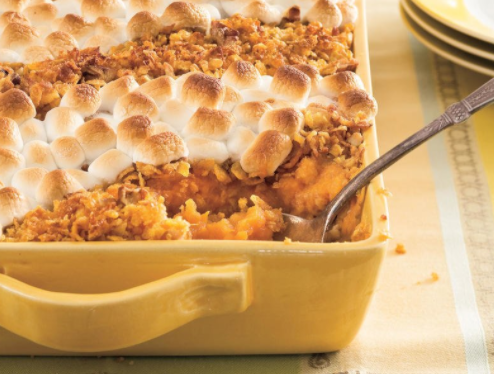 Closeup of the corner of a yellow casserole dish filled with sweet potatoes and topped with toasted marshmallows