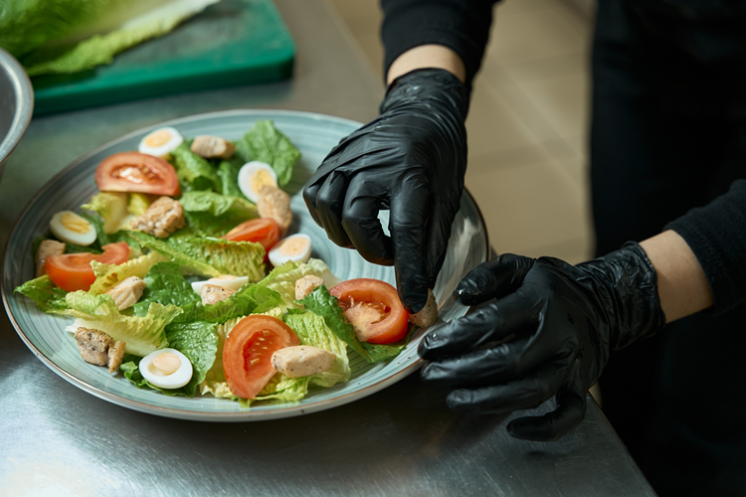 gloved hands arranging food on a blue plate with lettuce, tomatoes, and hardboiled eggs