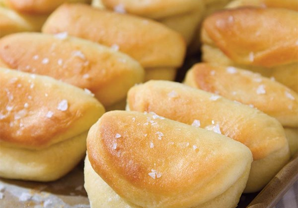 Closeup of a pan of folded. golden brown Parker House rolls sprinkled with flaky salt