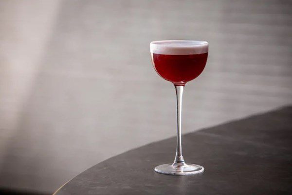 a single elegant small couple cocktail glass holding a garnet colored liquid with a small amount of froth on top