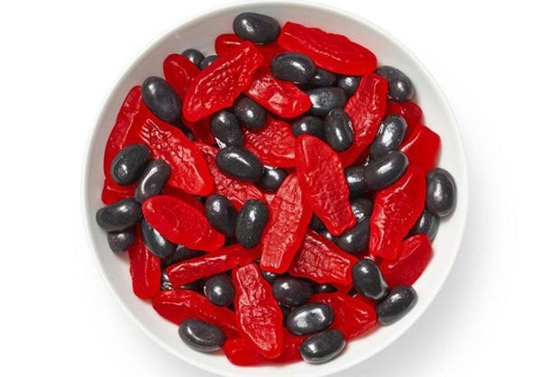 white bowl on a white background with red Swedish fish candy and black licorice jelly beans