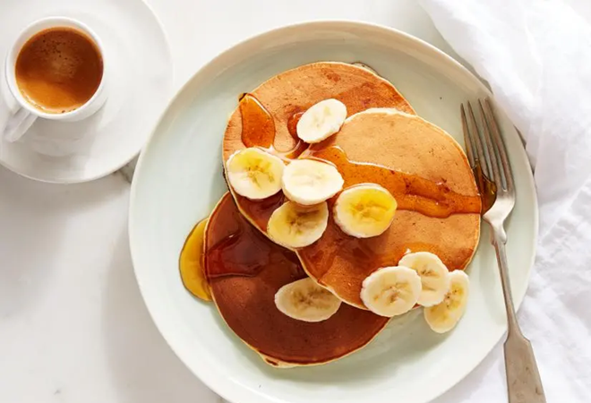 stack of three pancakes topped with slices of banana and syrup on a white plate